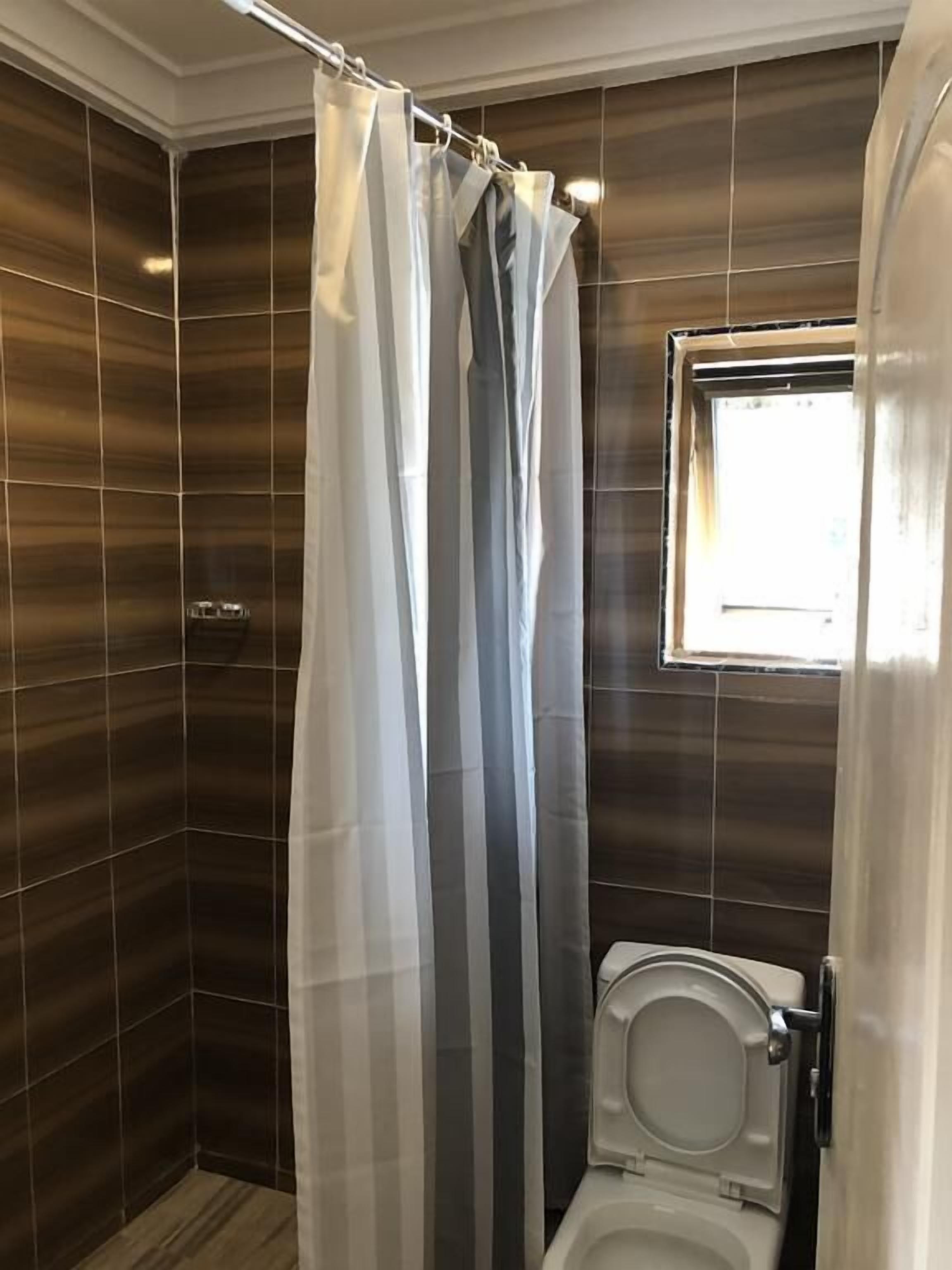 A bathroom with a shower curtain, a toilet, and a window.