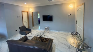 Una sala de estar moderna con ventilador de techo, televisor de pantalla plana y una zona de estar con sofá y sillones.