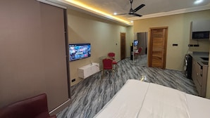 Habitación de hotel con una cama, televisor montado en la pared, ventilador de techo y un pequeño rincón de descanso con una mesa y sillas.