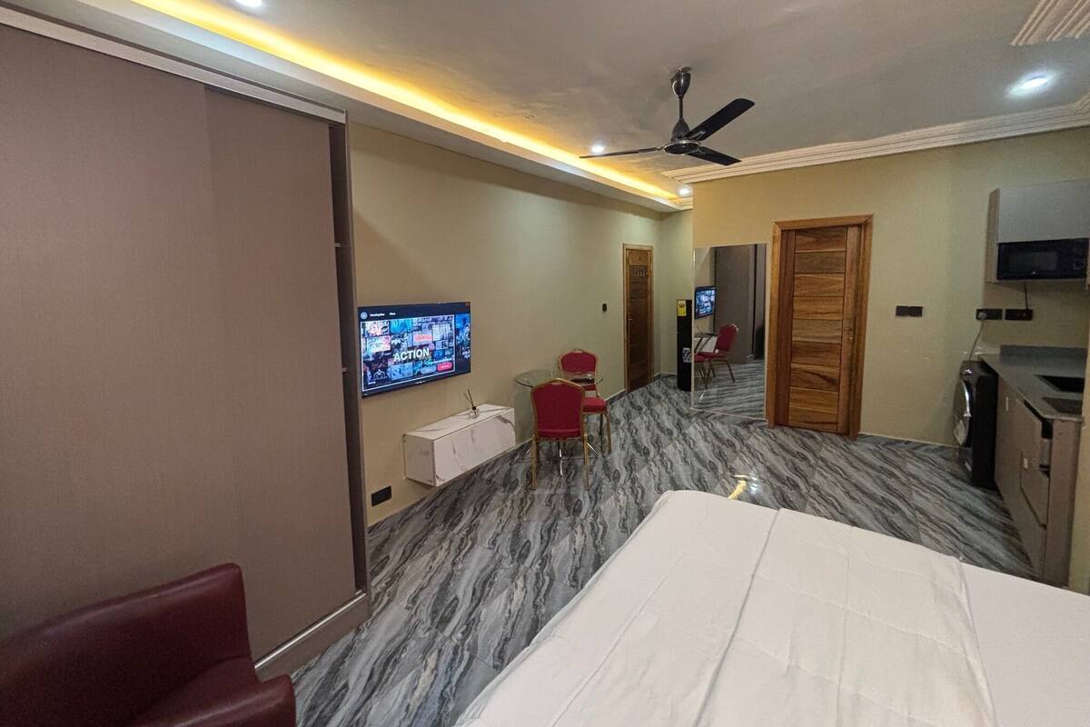 Ein Hotelzimmer mit einem Bett, einem an der Wand befestigten Fernseher, einem Deckenventilator und einer kleinen Sitzecke mit Tisch und Stühlen.