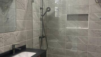 A modern bathroom with a glass-enclosed shower, a sink with a black countertop, and marble tiles.