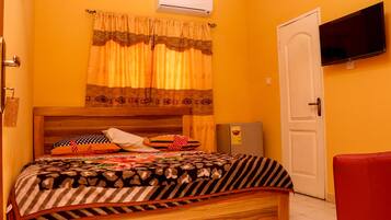 Une chambre à coucher avec un lit en bois, une chaise rouge, un téléviseur fixé au mur et un appareil de climatisation.
