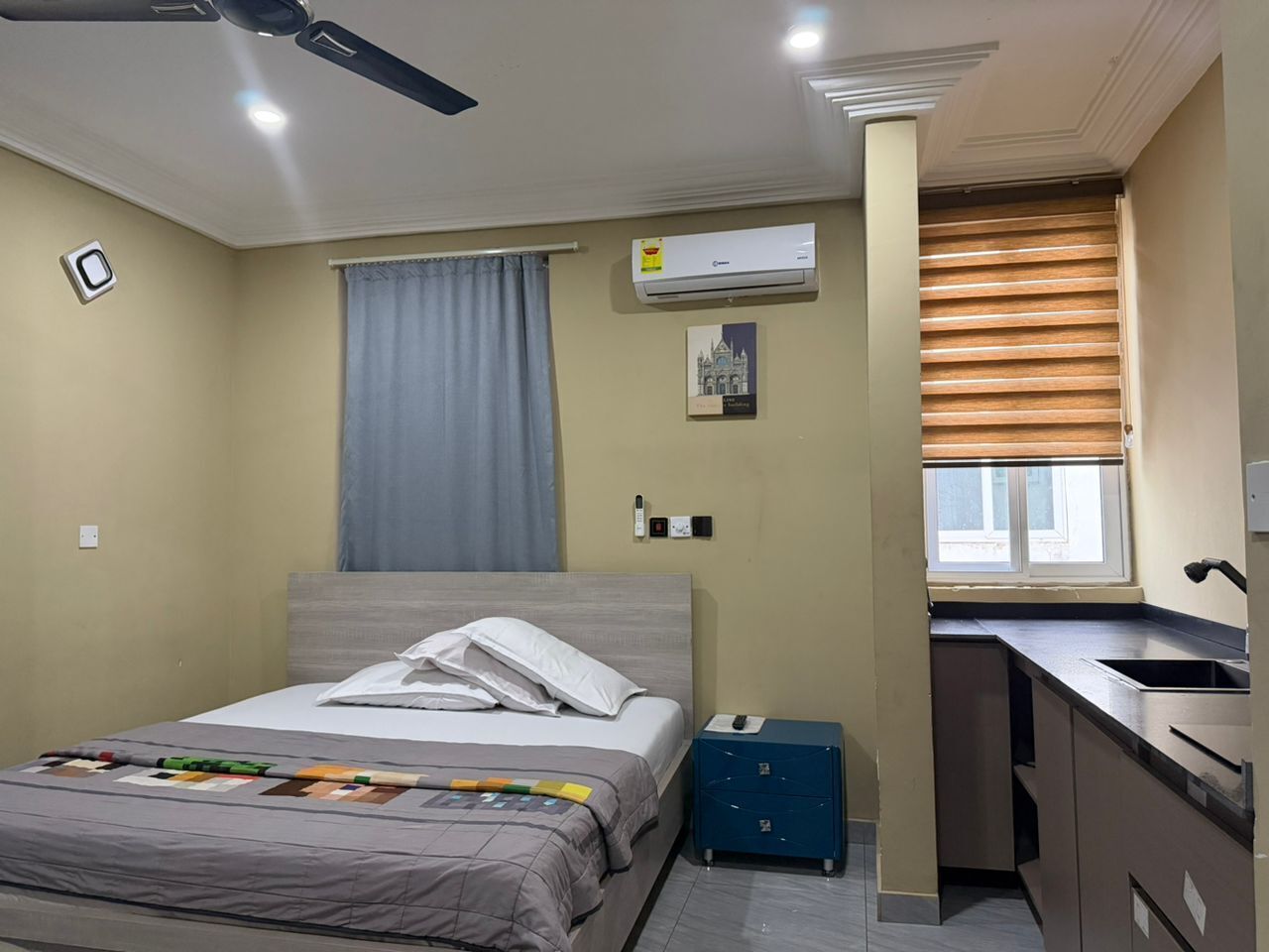 Un dormitorio con cama, escritorio, ventana con persianas, aire acondicionado y ventilador de techo.