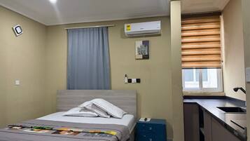 Un dormitorio con cama, escritorio, ventana con persianas, aire acondicionado y ventilador de techo.