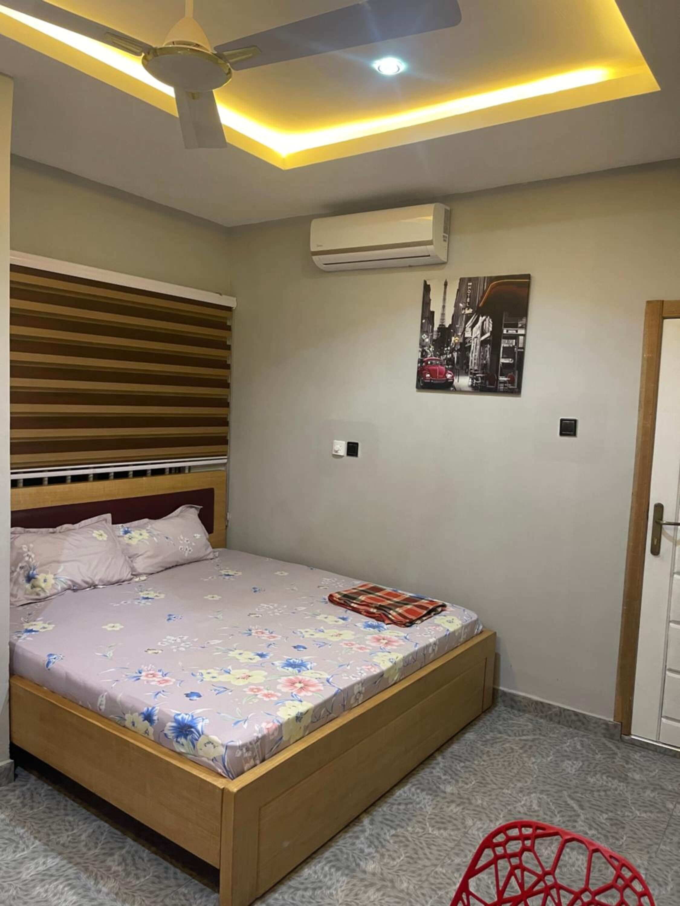 Ein Schlafzimmer mit Bett, Deckenventilator, Klimaanlage, einem Poster an der Wand und einer Tür.