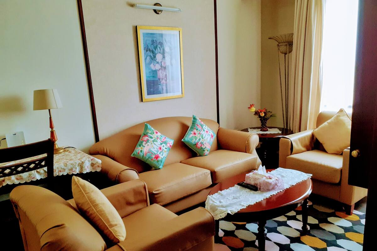 A living room with two brown leather sofas, a small table with a lace tablecloth, and a colorful patterned floor.