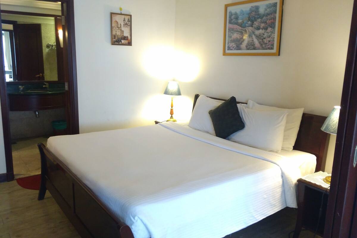 A neatly made bed with white linens, a bedside lamp, and a painting on the wall.