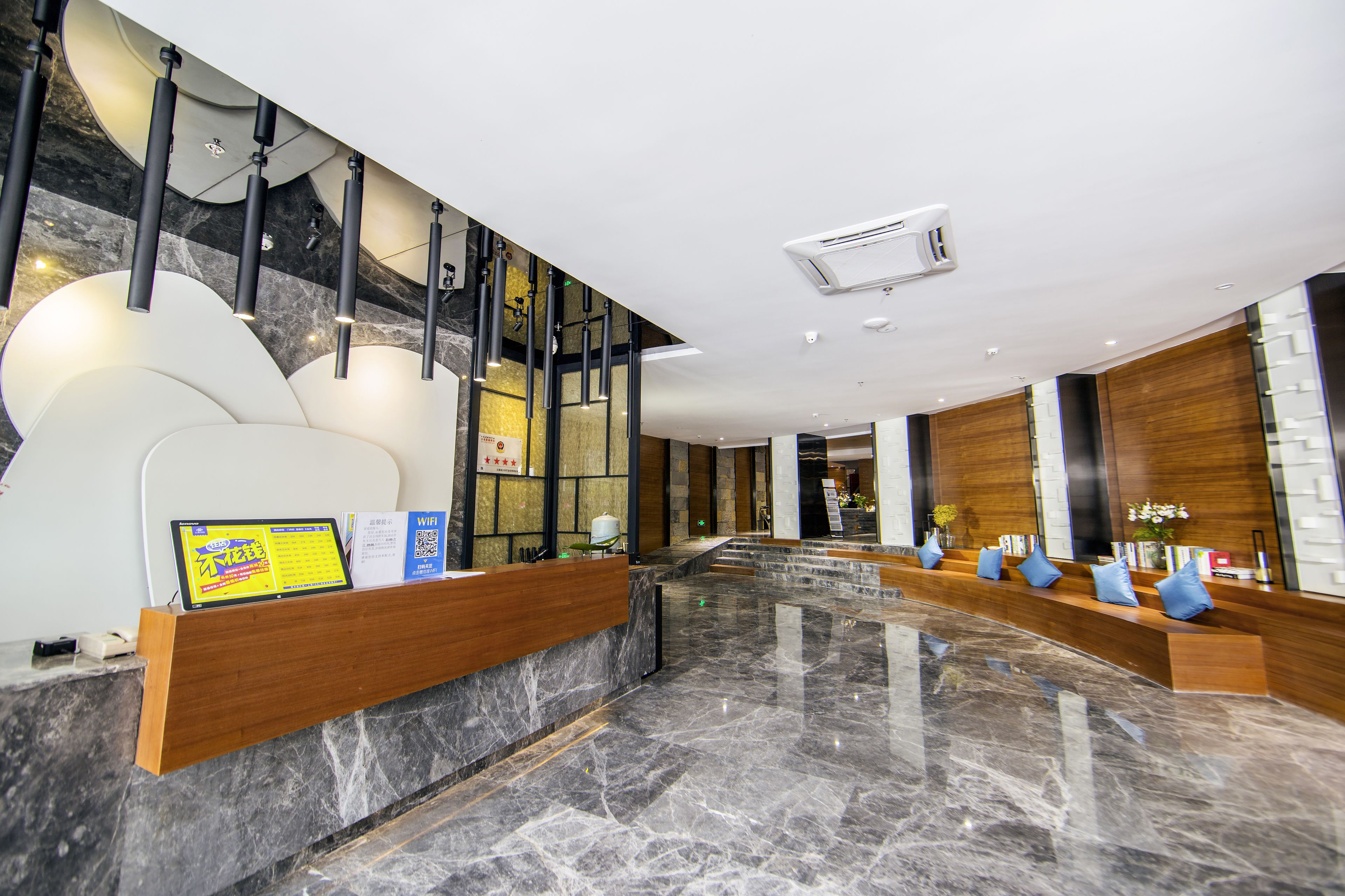 A modern lobby with a marble floor, wooden reception desk, and a seating area with blue cushions.