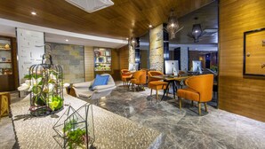 A modern lobby with wooden ceiling, stone walls, and a marble floor. There are several orange chairs and a white sofa. - Yunman Hotel Kunming Donghua (Kunming)