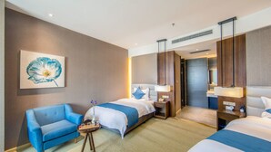 Quarto de hotel com duas camas, uma poltrona azul, uma mesinha com um vaso de flores e um quadro de uma flor na parede.