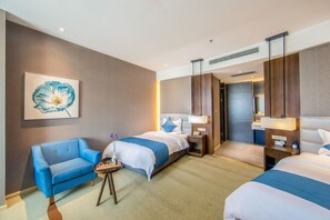 A hotel room with two beds, a blue armchair, a small table with a vase of flowers, and a painting of a flower on the wall. - Yunman Hotel Kunming Donghua (Kunming)