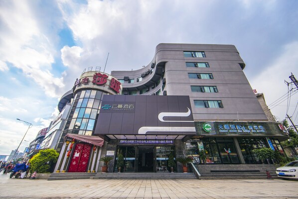 A modern hotel with a curved facade, large windows, and a prominent entrance with a red door. - Yunman Hotel Kunming Donghua (Kunming)
