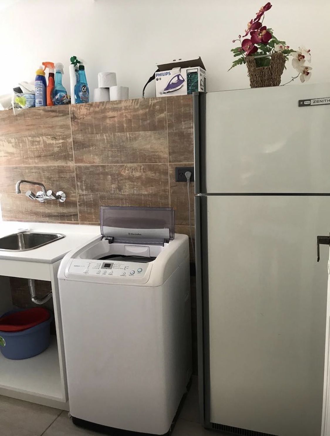 Eine kompakte Küche mit integrierter Waschmaschine und Trockner, einem Spülbecken und einem kleinen Kühlschrank.
