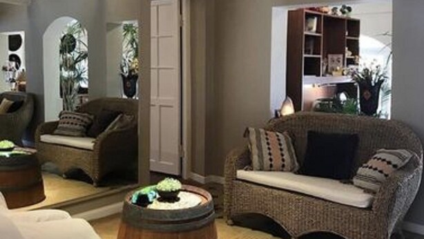 Una sala de estar acogedora con un sofá de mimbre, una mesa redonda de madera y un espejo grande que refleja la habitación.