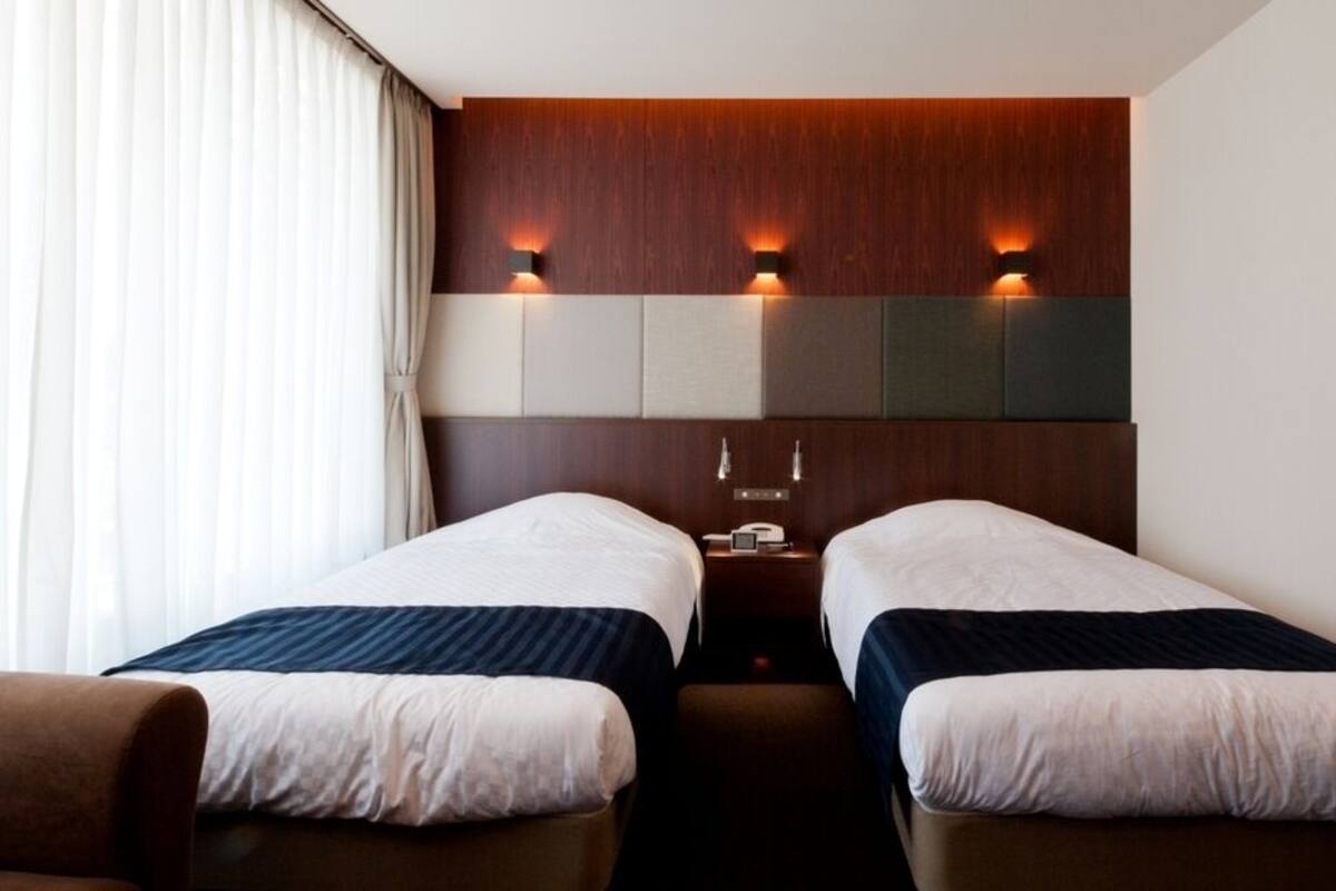 Ein Hotelzimmer mit zwei Einzelbetten, einem hölzernen Kopfteil, Wandleuchten und einem Nachttisch.
