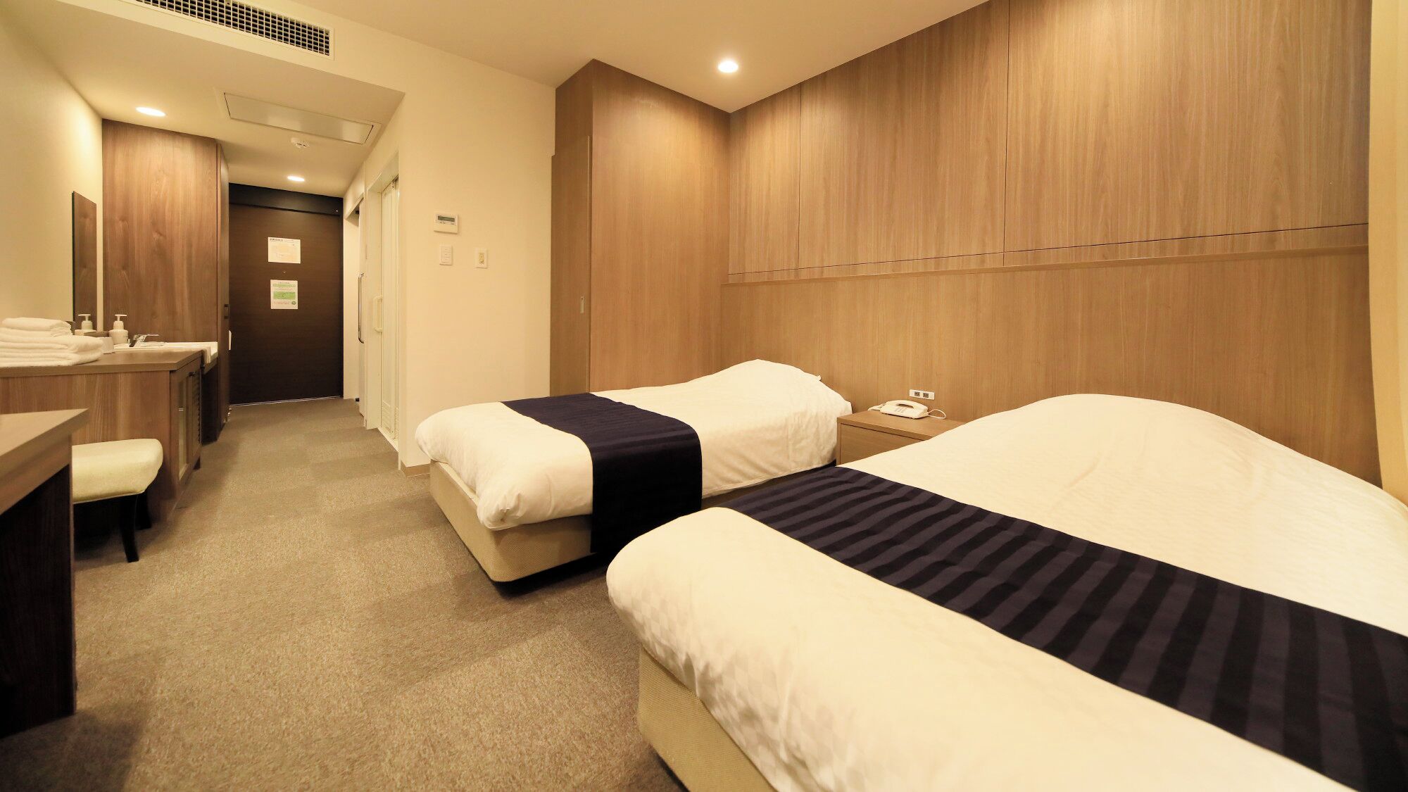 A hotel room with two beds, a desk with a chair, and a bathroom visible through an open door.