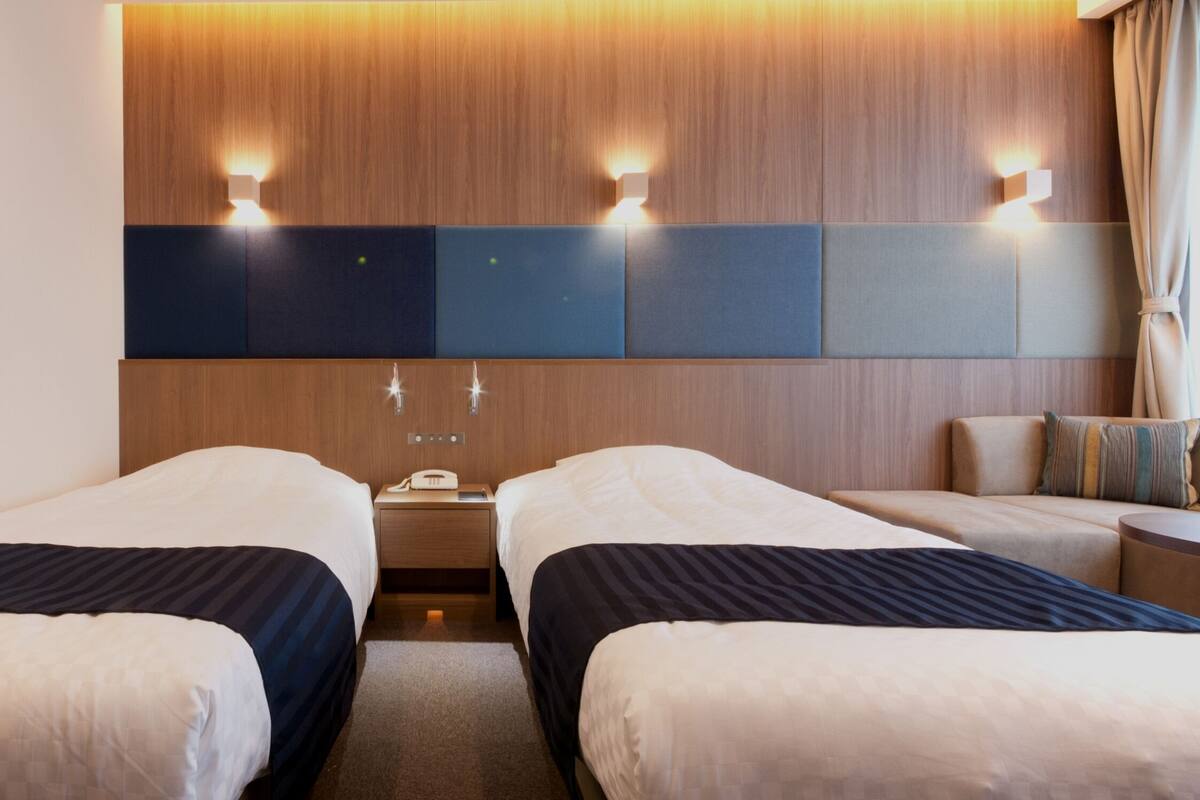 Ein Hotelzimmer mit zwei Betten, einem Holzkopfende, einem Nachttisch mit Telefon und Lampe sowie einer Sitzecke mit Sofa und Sesseln.