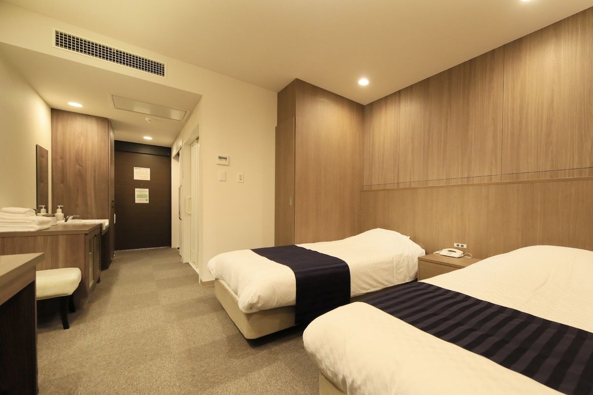 A hotel room with two beds, a desk, a chair, a mirror, and a wardrobe.