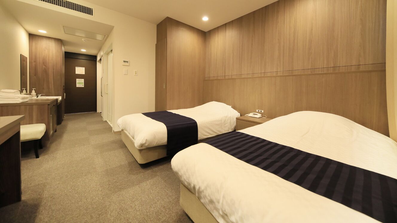 A hotel room with two beds, a desk, a chair, a mirror, and a wooden headboard.