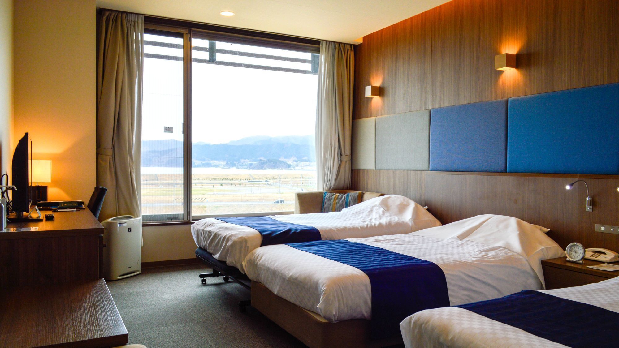 A hotel room with two beds, a desk with a computer, a lamp, and a view of the airport.