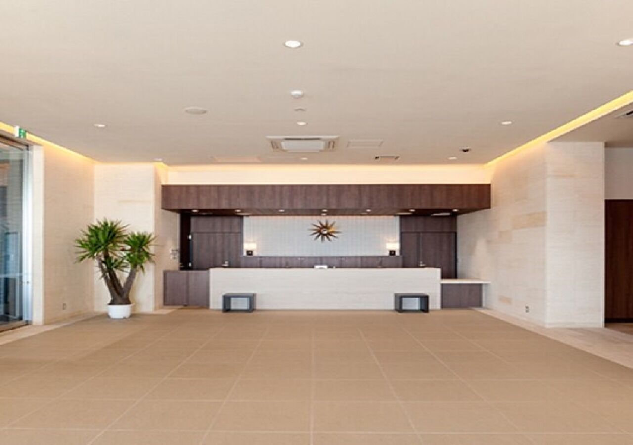 A spacious lobby with a reception desk, a decorative wall piece, and a potted plant.