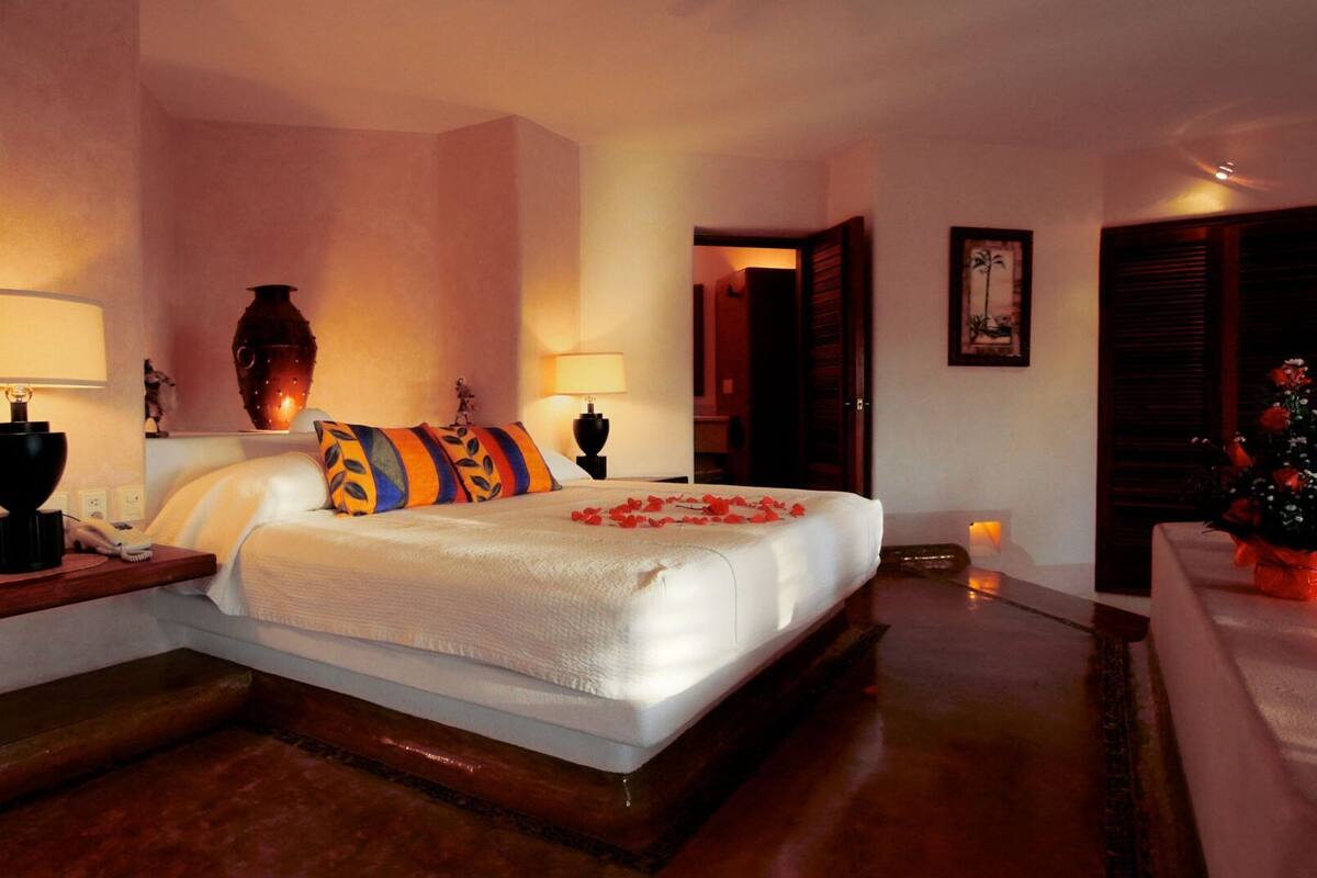 Ein Hotelzimmer mit einem großen Bett, zwei Nachttischen mit Lampen, einer Vase und einem kleinen Tisch mit Blumen.