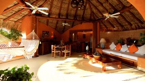 A spacious living area with a thatched roof, a hammock, a wooden sofa with orange cushions, and a dining area with a table and chairs. - Villa Carolina Boutique Hotel (Zihuatanejo)