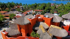 A resort with thatched-roof buildings, a sign reading "Villa Carolina Boutique Hotel," and a view of the ocean. - Villa Carolina Boutique Hotel (Zihuatanejo)