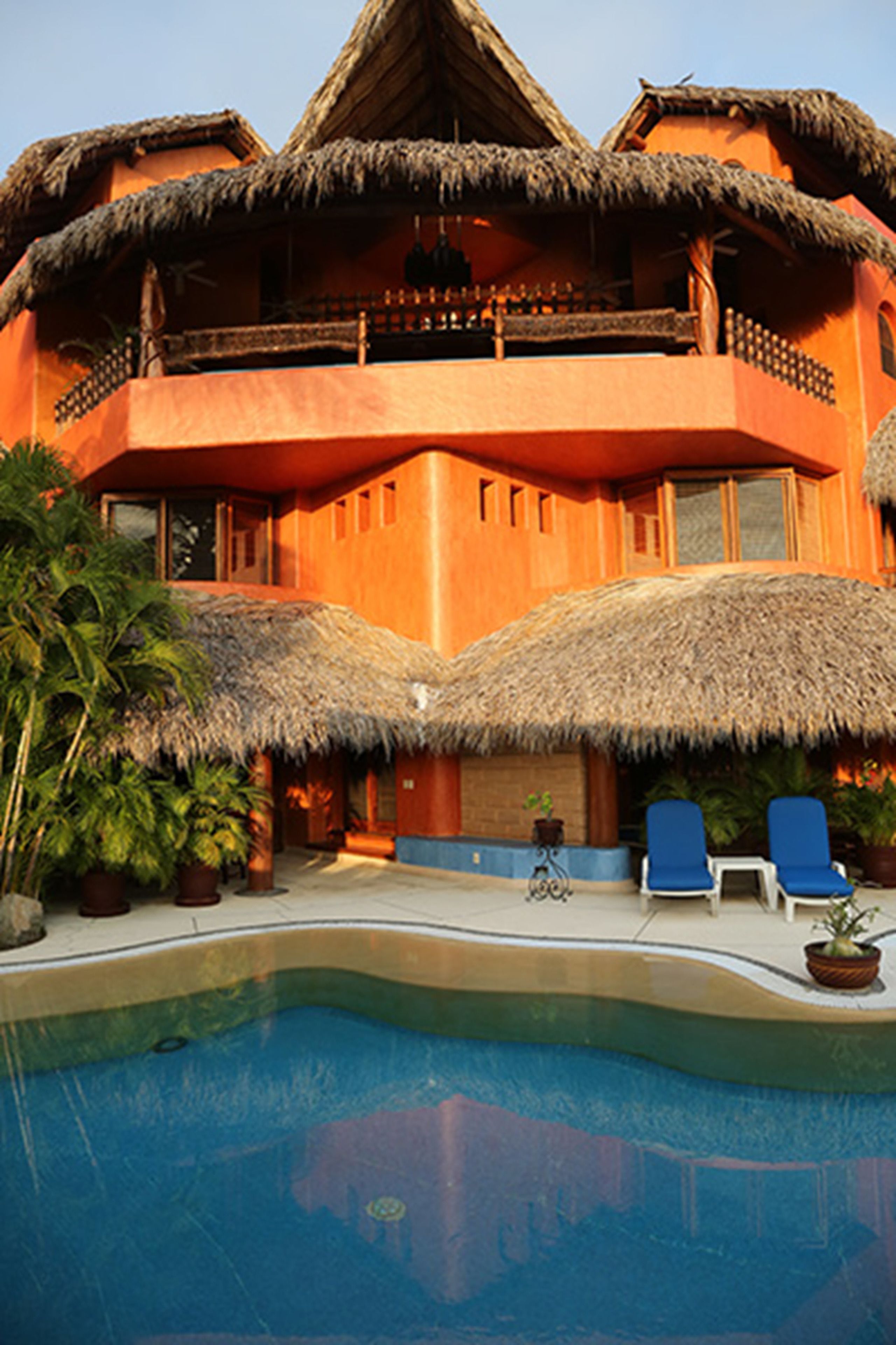 A resort with a pool, thatched-roof buildings, and lounge chairs.
