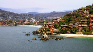 A coastal resort with beachfront villas, rocky outcrops, and a mountainous backdrop. - Villa Carolina Boutique Hotel (Zihuatanejo)