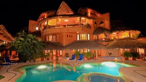 Ein Resort mit Pool, strohgedeckten Gebäuden und Liegestühlen.
