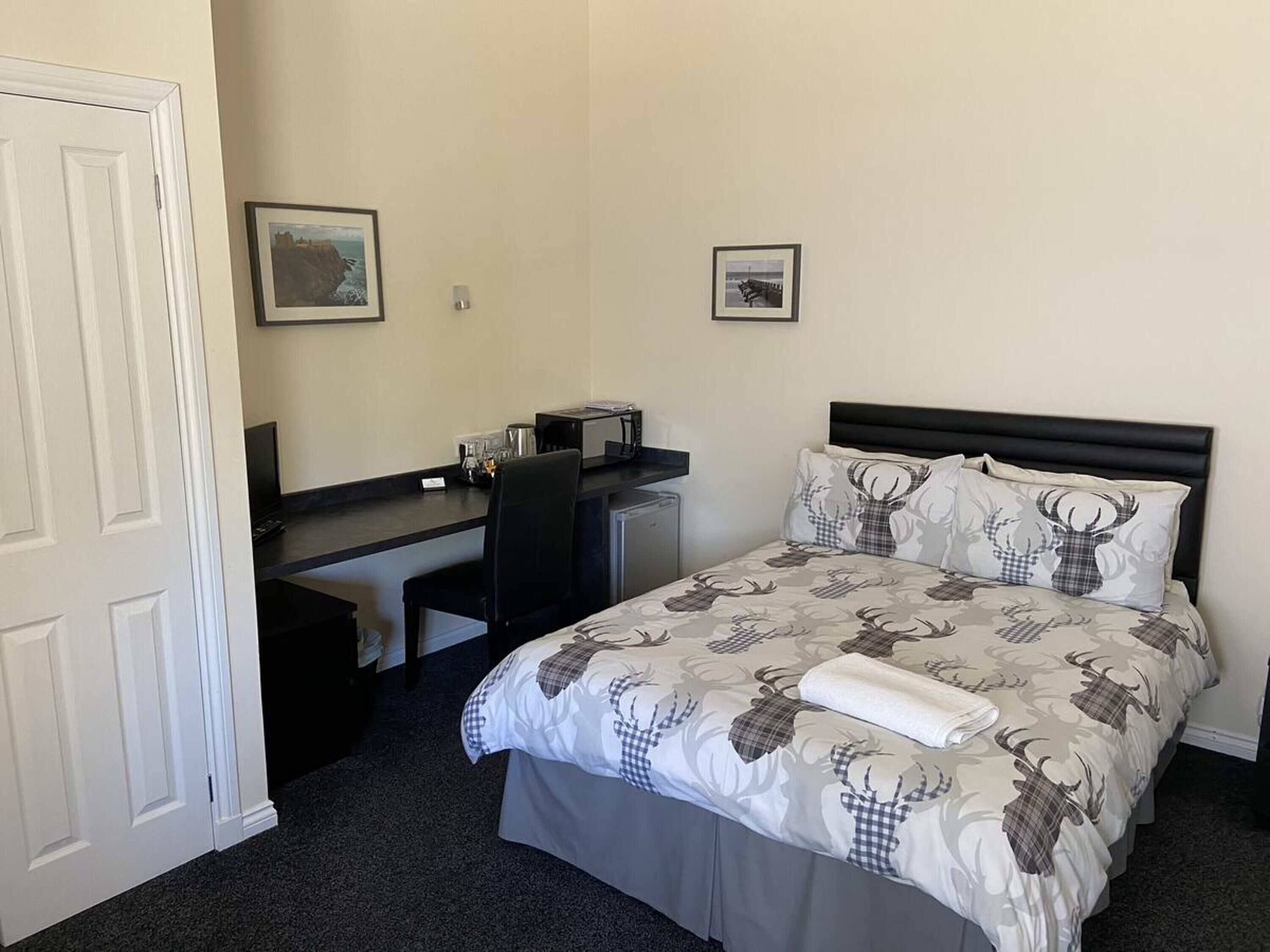 A hotel room with a bed, a desk, and two framed pictures on the wall.
