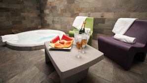 Een wellnessruimte met een jacuzzi, een tafel met fruit en drankjes, en een paarse fauteuil.