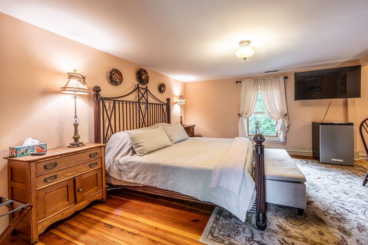 A bedroom with a wooden bed, bedside tables, a dresser, a bench, a television, and a window with curtains.