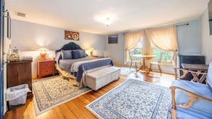 Quarto com cama, mesas de cabeceira, escrivaninha, cadeira e janela com cortinas.