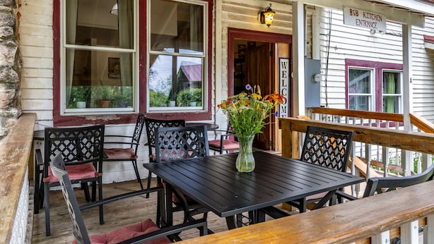 Um deck de madeira com mesa e cadeiras, um vaso com flores e uma placa indicando "B&B KITCHEN ENTRANCE".