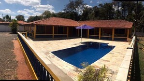 Una piscina con bordo piastrellato, zona relax coperta e giardino recintato.