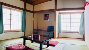 Une pièce de style japonais traditionnel, avec un sol recouvert de tatamis, une petite table basse entourée de coussins, un téléviseur et un petit meuble.