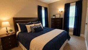 Une chambre à coucher bien rangée, avec un lit, des tables de chevet, une commode et une lampe fixée au mur.