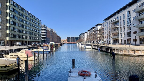 Ein Kanal mit an beiden Seiten vertäuten Booten, gesäumt von modernen Gebäuden mit Balkonen.