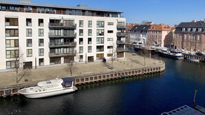 Ein modernes Mehrfamilienhaus mit mehreren Balkonen, einem Kanal und angestaubten Booten in der Nähe.