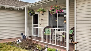 Een veranda met een witte balustrade, rieten stoelen, hangmanden met bloemen en een beeldje van een jongen met een waterkan.