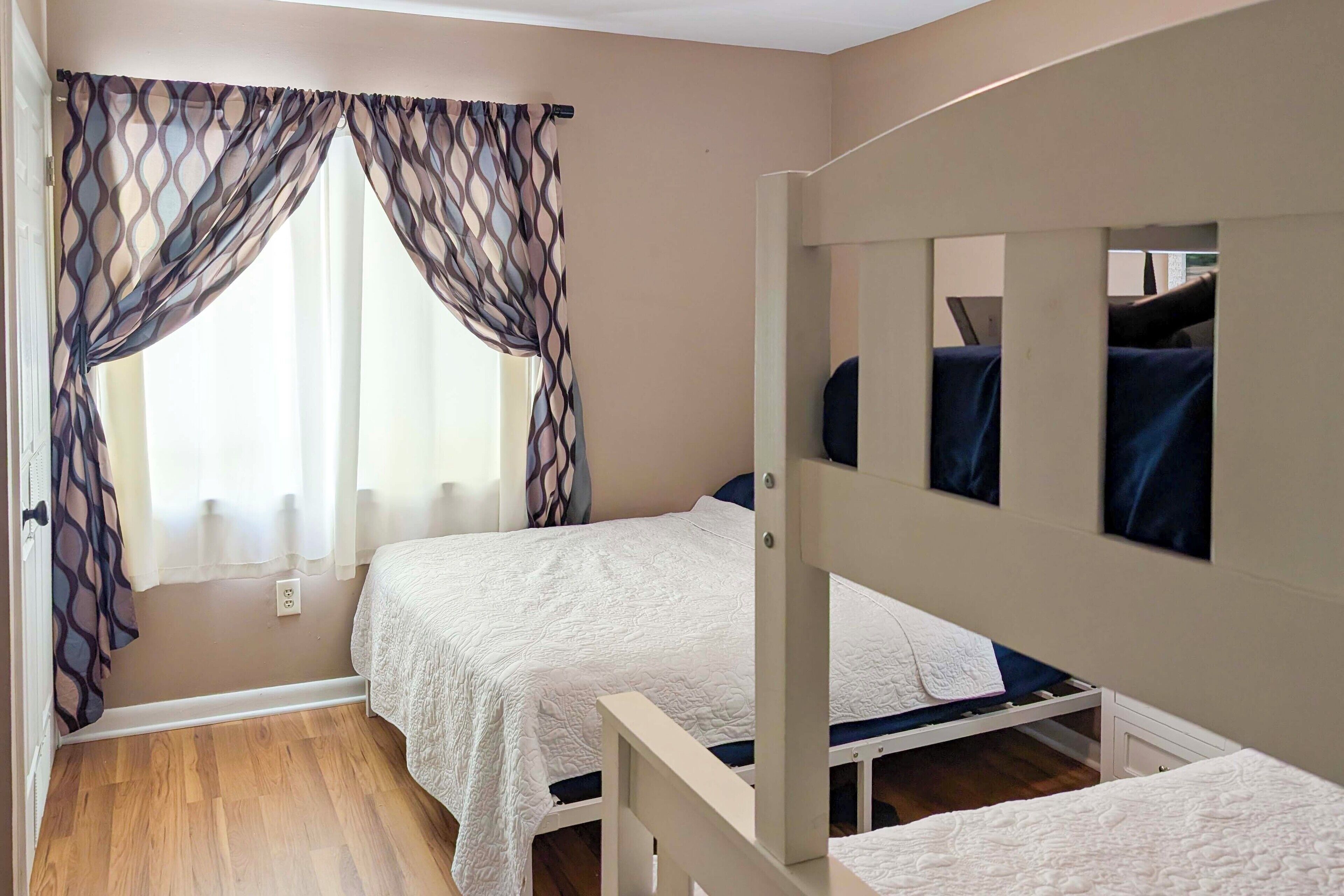 Un dormitorio con dos camas, una ventana con cortinas translúcidas y un espejo en la pared.