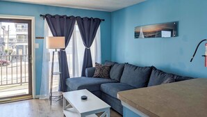 A room with a blue wall, a sofa, a white table, a lamp, and a painting. - Coastal Condo w/ Pool, 1 Block to Wildwood Beach! (Wildwood)