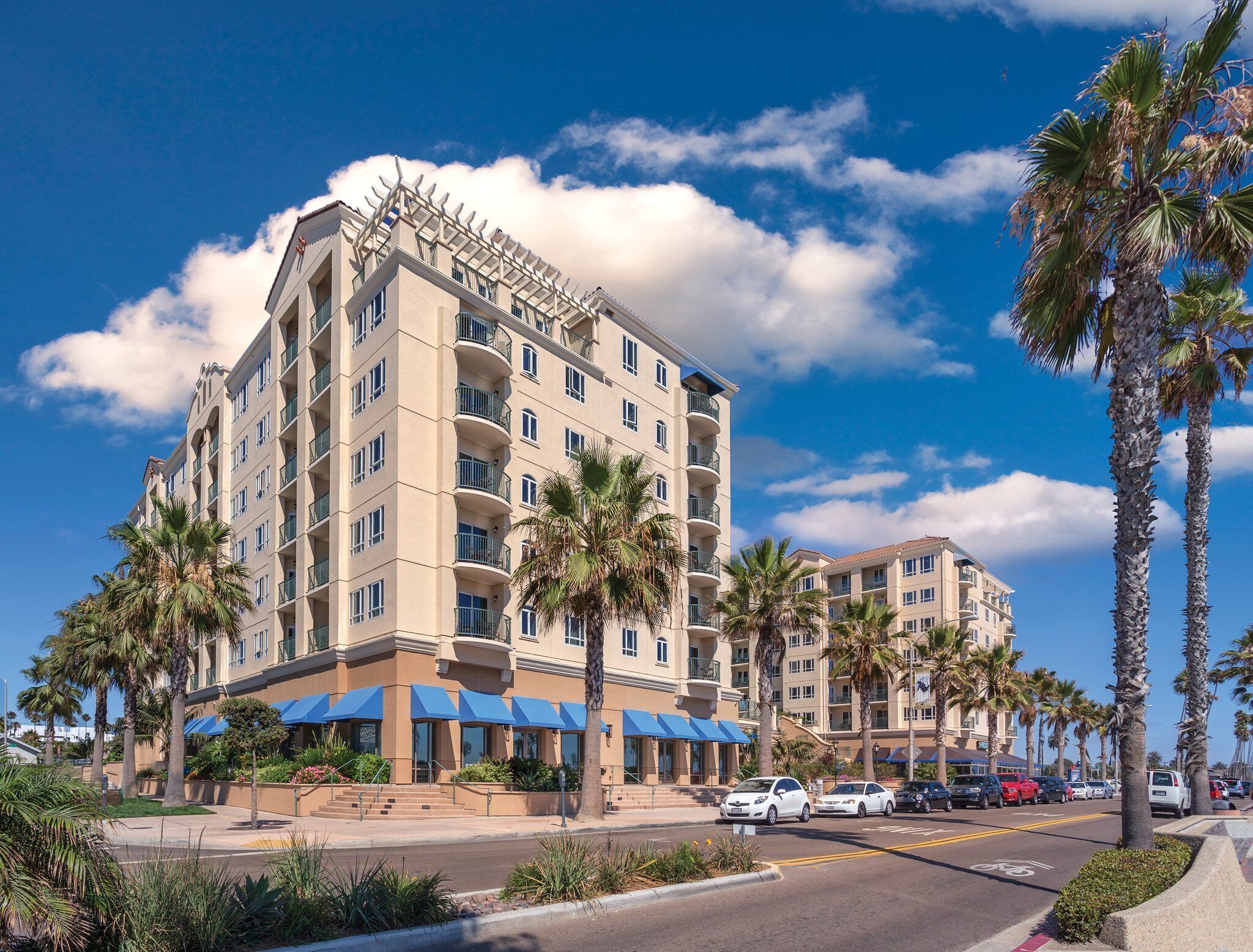 A multi-story hotel with balconies, palm trees, and a clear blue sky.