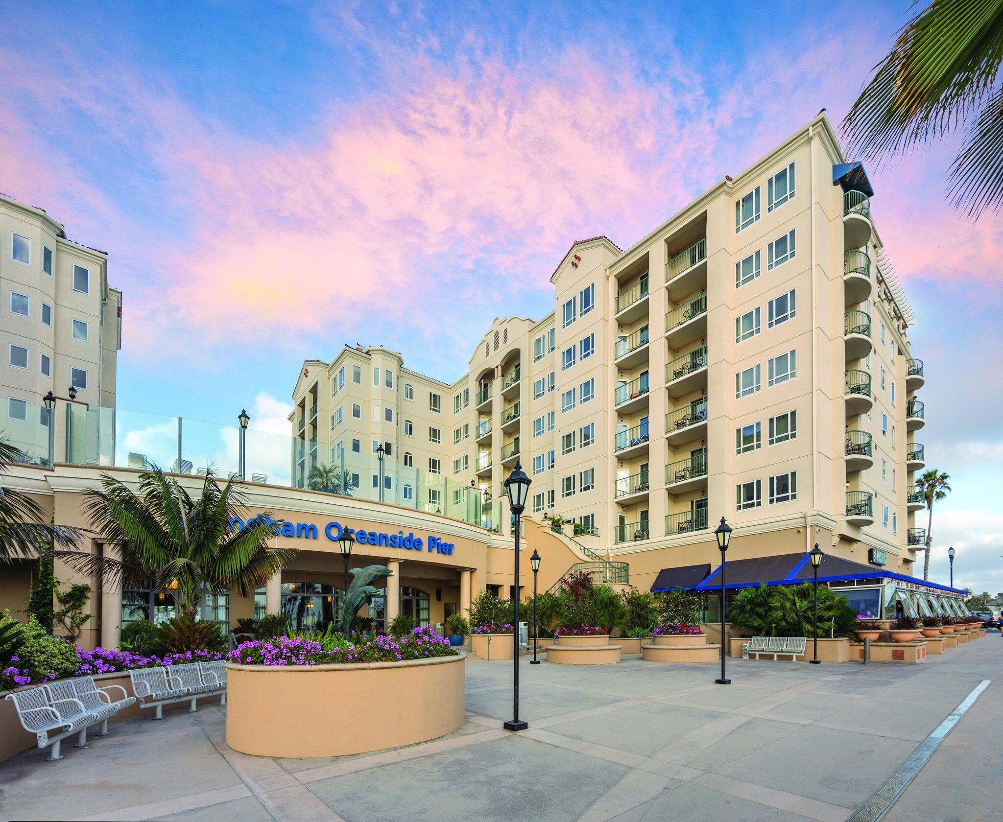 A hotel with a modern design, featuring a central courtyard with benches and planters, and a sign that reads "Oceanside Plaza."
