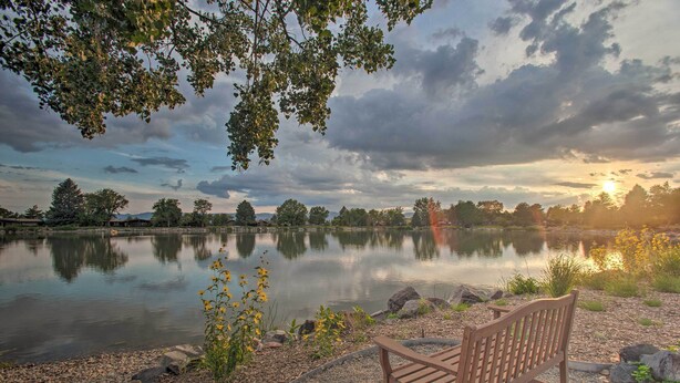 Un banc au bord d’un lac paisible, entouré d’arbres, sous un ciel nuageux.