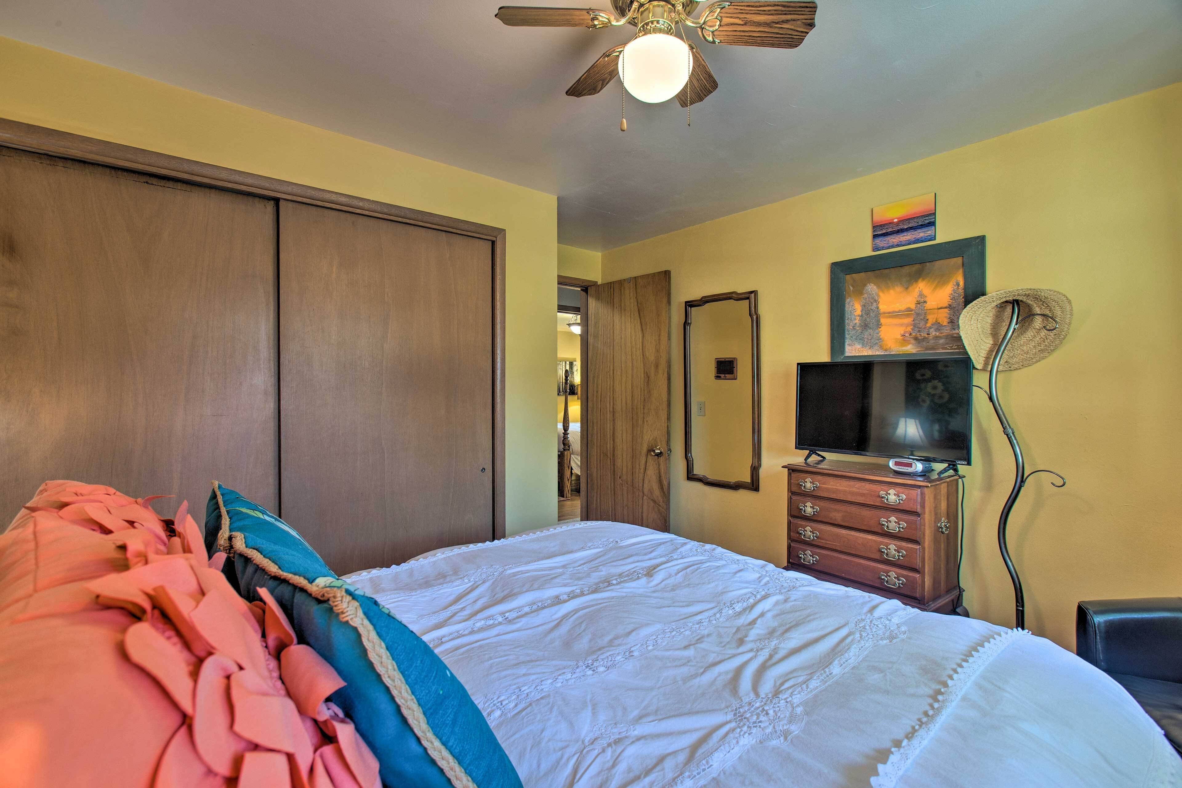 A bedroom with a bed, a dresser, a ceiling fan, and a door leading to another room.