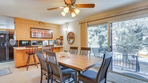 Une cuisine moderne avec des meubles en bois, un coin repas doté d’une grande table et de chaises, et une vue sur un paysage enneigé par de grandes fenêtres.
