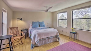 Un dormitorio con cama, una silla, una mesa, una lámpara de pie y ventanas amplias.